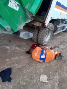 A Garbage Collector's Head Is Crushed Under The Lid Of A Garbage Collection Vehicle